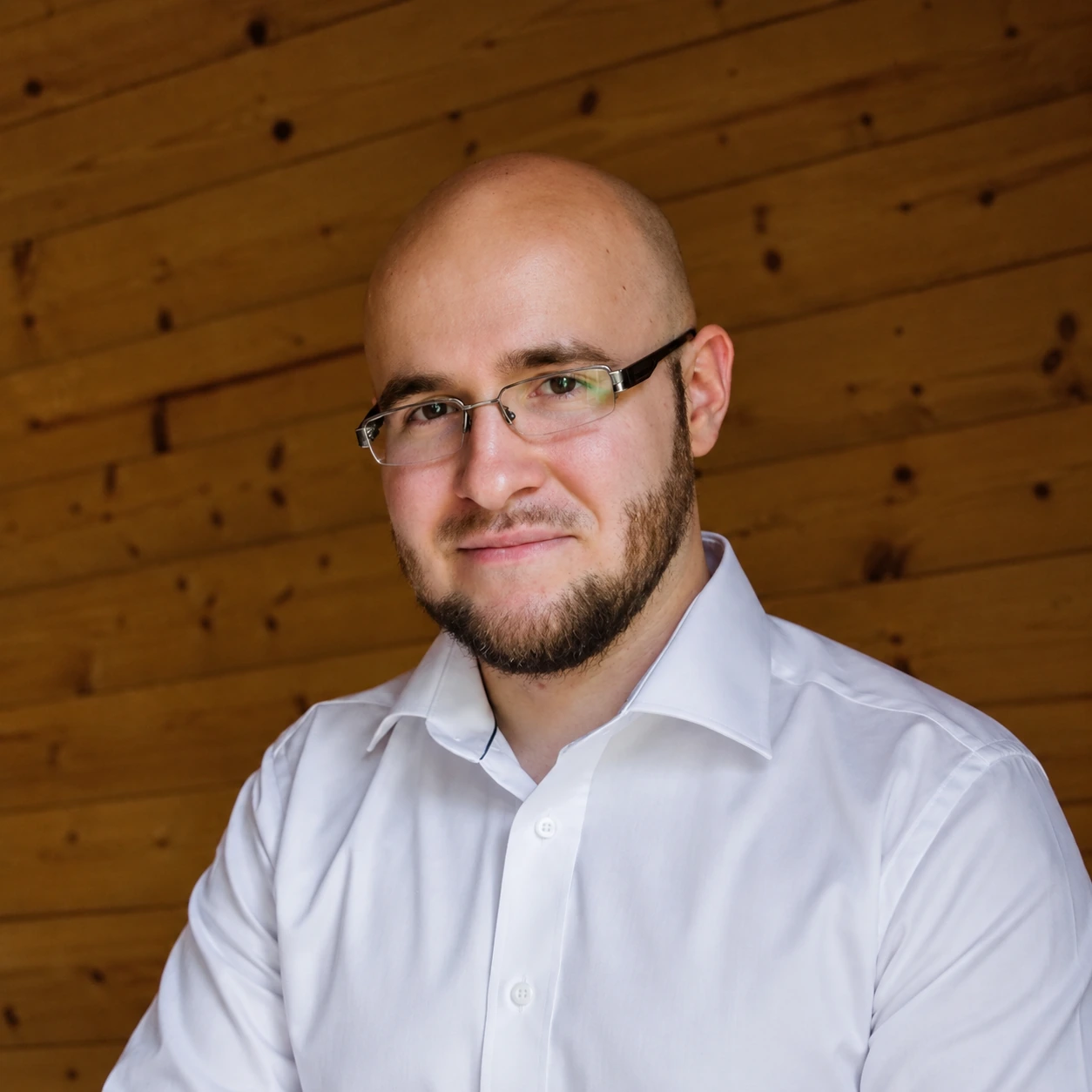 Marcin Szczepanik w białej koszuli na tle drewnianej ściany